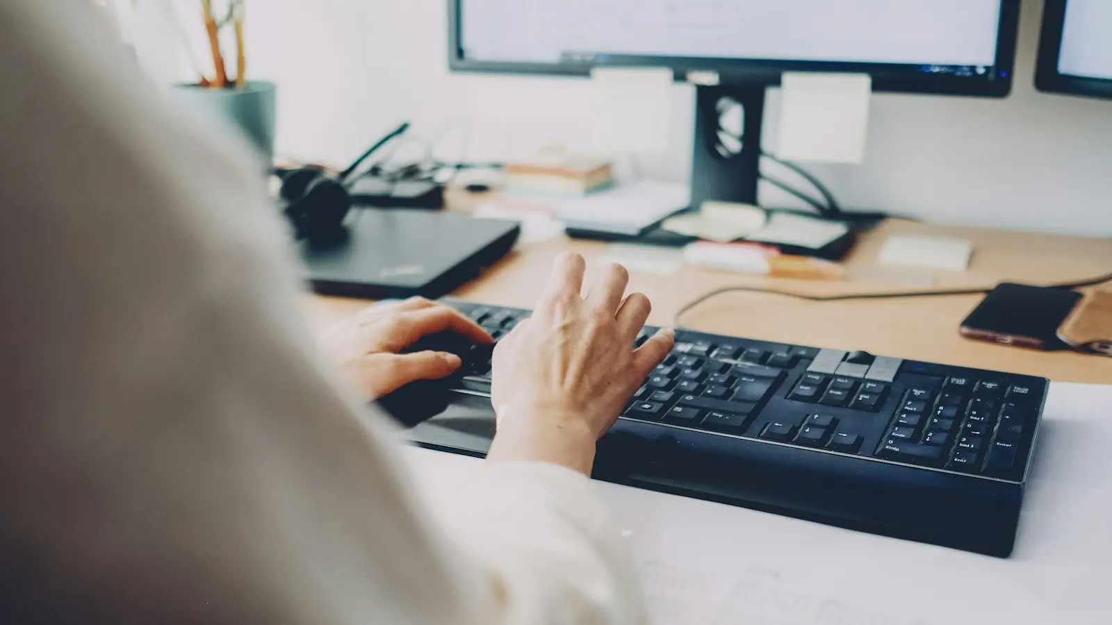 Hände beim Tippen auf einer Tastatur am Schreibtisch – RSI und Mausarm vorbeugen