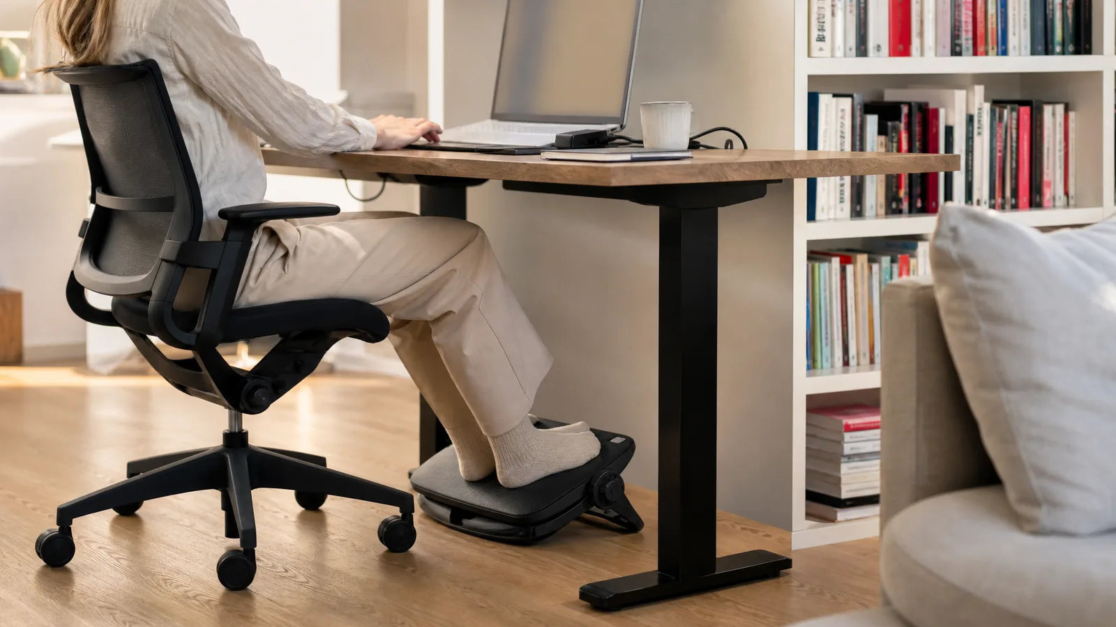 Füße in Socken oder Hausschuhen ruhen auf einer ergonomischen Fußstütze mit Wippe unter dem Schreibtisch, flache Perspektive knapp über dem Boden – Symbolbild zu «Fußstütze: Die 4 besten ergonomischen Modelle im Vergleich»